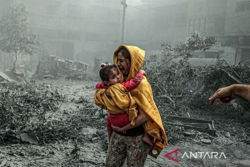 Seorang perempuan sambil menggendong anak bereaksi setelah serangan udara Israel menghantam sebuah kawasan di Kota Gaza, Palestina (23/10/2023). (ANTARA/Anadolu/Ali Jadallah/pri.)