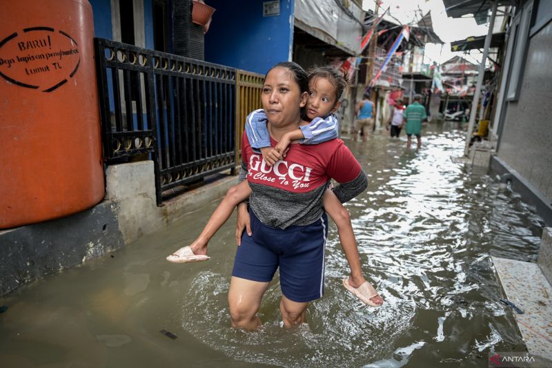 Seorang warga menggendong anaknya di tengah banjir rob di Muara Angke, Jakarta, Jumat (13/12/2024). (ANTARA FOTO/Fauzan)
